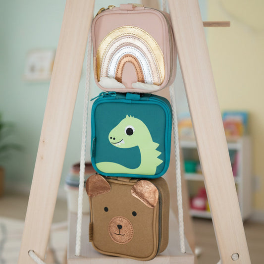 Drei littlebag Erste-Hilfe-Taschen für Kinder übereinandergestapelt im Kinderzimmer: Regenbogen, Dino und Bär